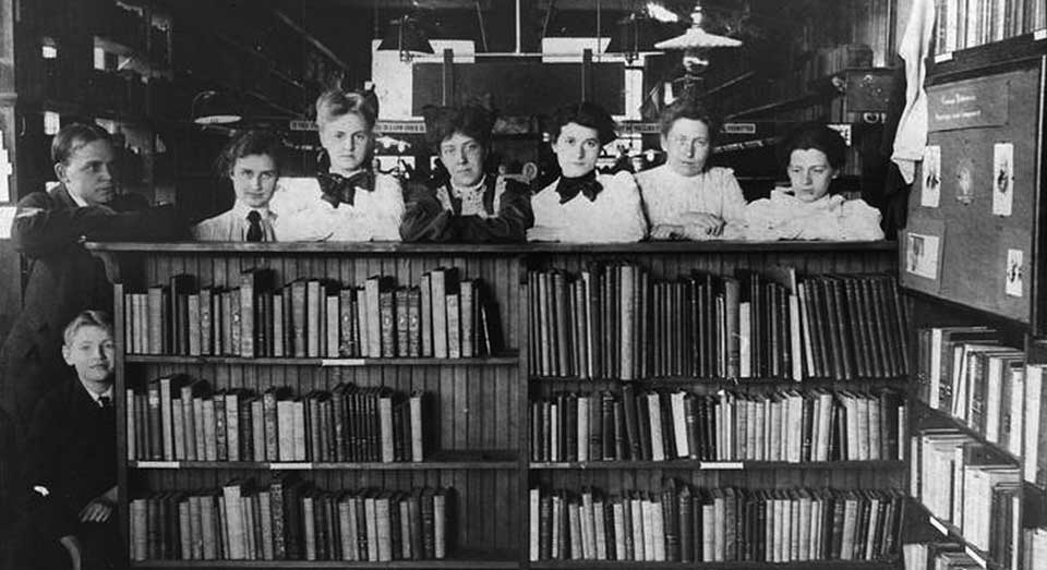 Librarians standing behind a bookcase in the early 20th century