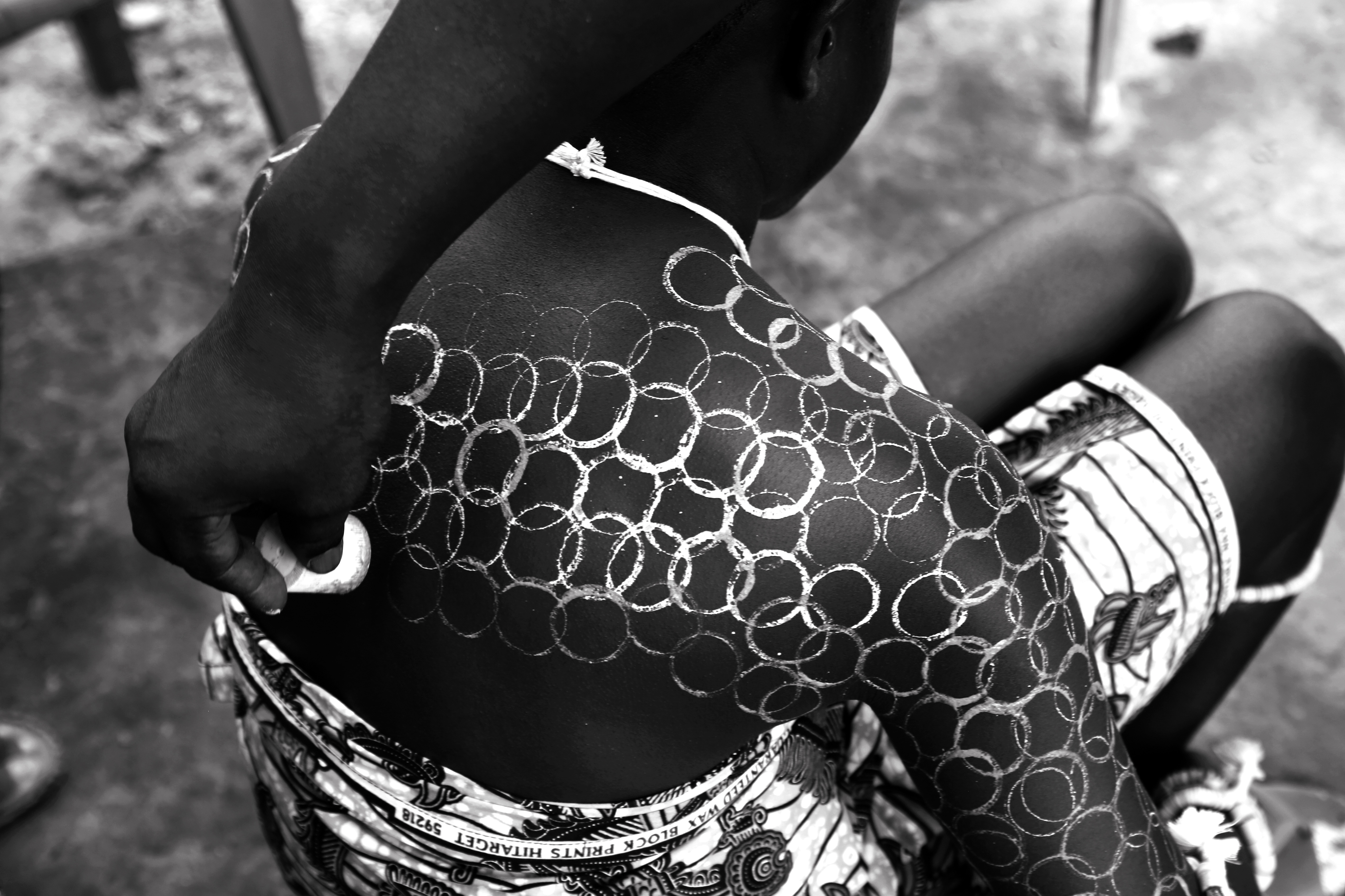 Brief Context: The Anlo Ewe concept of Nugbidodo (reconciliation) is central to maintaining social order and spiritual harmony. Within Anlo Ewe cosmology, ancestral favor is hinged  on social harmony. As such, it is believed that unresolved conflicts and misunderstandings provoke ancestral displeasure, manifesting as communal ill-health, potential calamities, or collective misfortune. Consequently, the practice of Nugbidodo is employed at all levels of society—within families, clans, married couples, and chieftaincies—to resolve disputes. The Nugbidodo rite is mostly performed by chiefs and elders who mediate and resolve disputes. This essential process of conflict resolution and reconciliation is a fundamental prerequisite for the successful celebration of the annual Hogbetsotso festival among the Ewe people.   Image description: Design process for body art on a young performer ahead of a funerary procession in honor of the late Torgbui Tenge Dzokoto Gligui VI during his burial ceremony at Anyako in the Volta Region of Ghana on the 29th of May 2021. Young girls whose bodies are decorated like this mostly perform during the Hogbetsotso festival. They usually accompany the entourage of chiefs in a procession and perform traditional dances, hence the need to pay their last respect to the chief of their village in a funerary procession to accompany him transition into the afterlife. Though the title of the image is not directly related to the actual Nugbidodo rite performed by Ewe elders, we are using the expression in relation to our peculiar situation—in a more abstract context to symbolize reconciliation, interdependence, and the significance of team work.