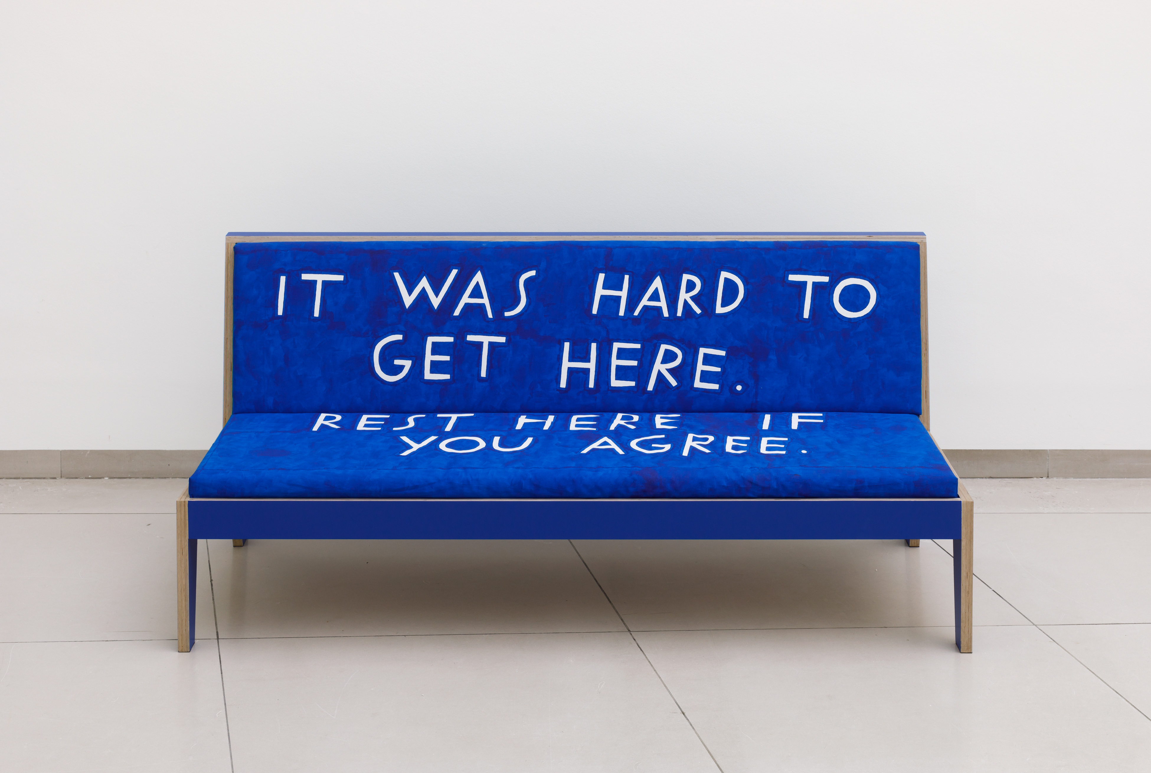 It is a blue sofa with the phrase "It was hard to get here. Rest here if you agree" written on it.