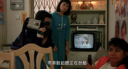 This is a still from the movie 富貴逼人 (It’s a Mad, Mad, Mad World, 1989), showing three people around a TV set, with one of them holding a video camera. A subtitle says ‘Daidi is playing cool.’ 